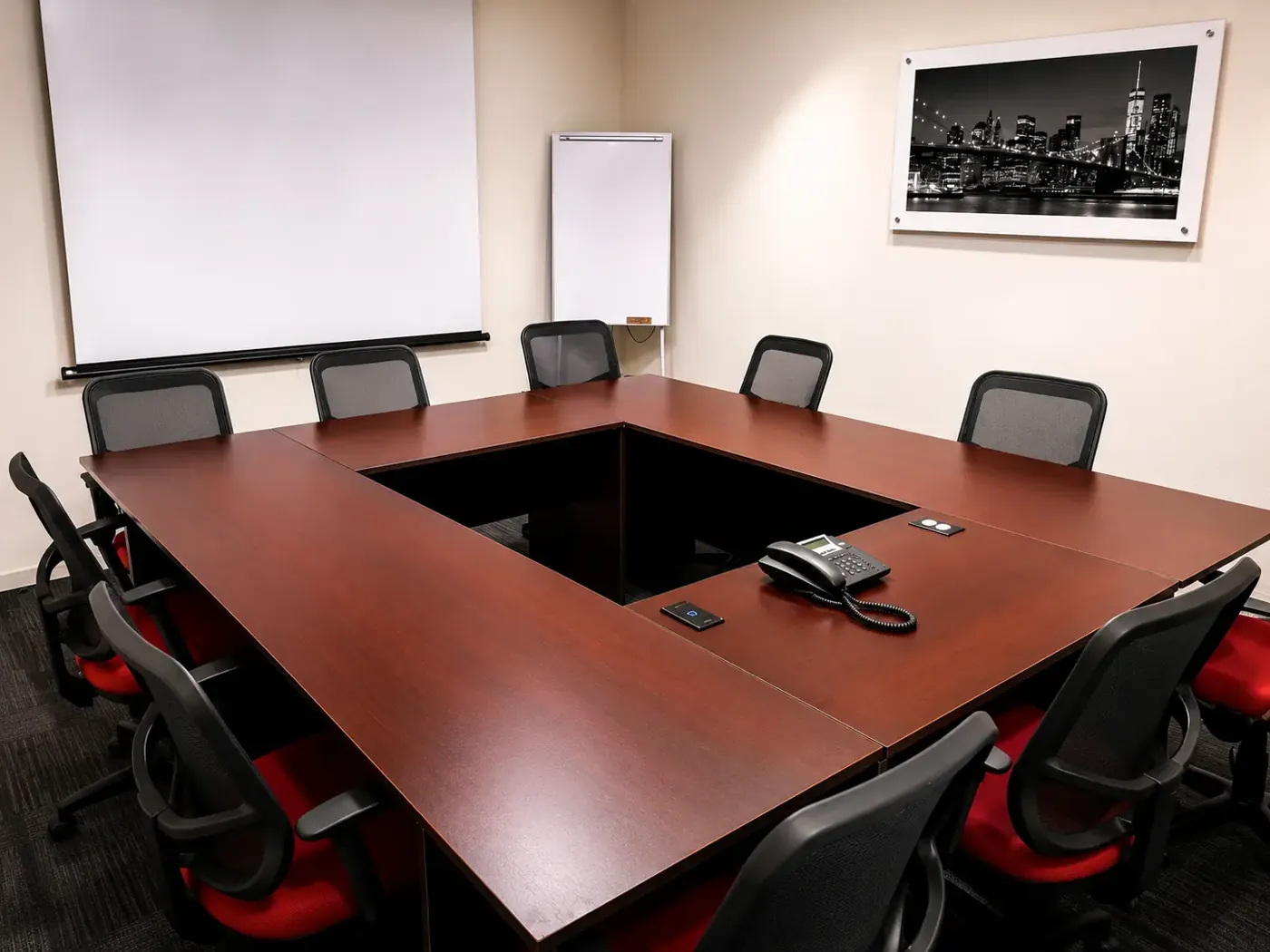 Sala de juntas con mesa para diez personas, pizarrón y pantalla de proyección
